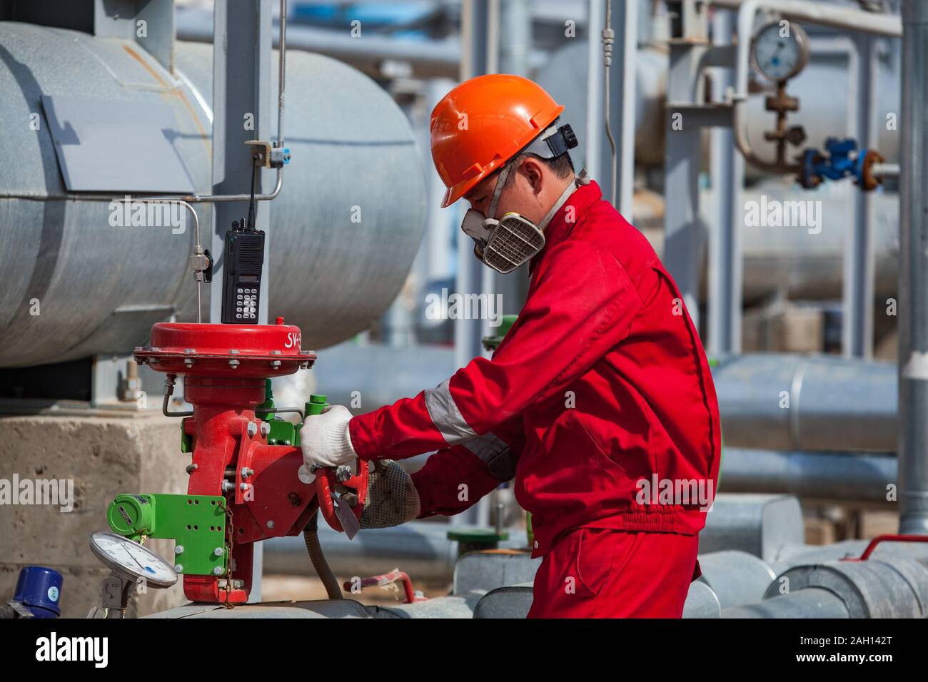 Worker in red protective work wear and gas mask and work wear and orange helmet on oil and gas refinery plant. Stock Photo