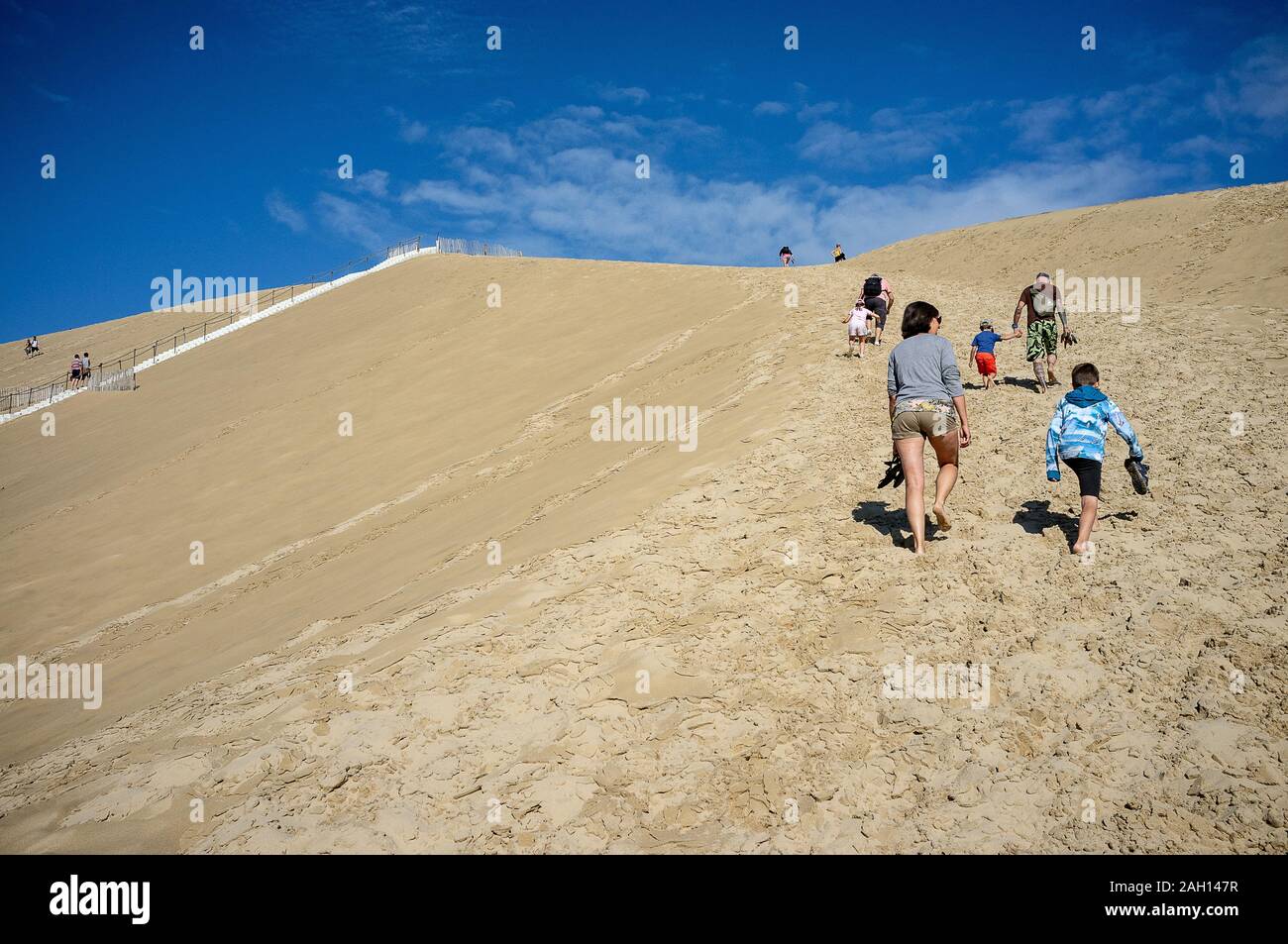 people climbing the dunes against blue sky with white clouds Stock Photo