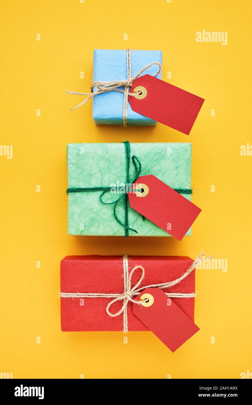Red, green and blue gift boxes with red gift tag on yellow background. Top view, copy space. Stock Photo