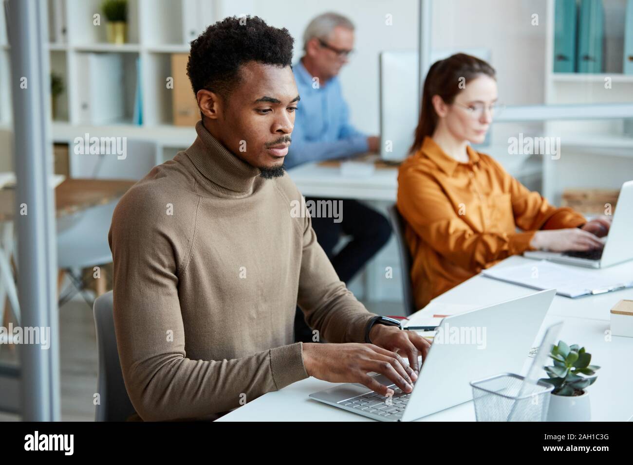 Multiethnic business people sitting on their workplaces and typing on ...