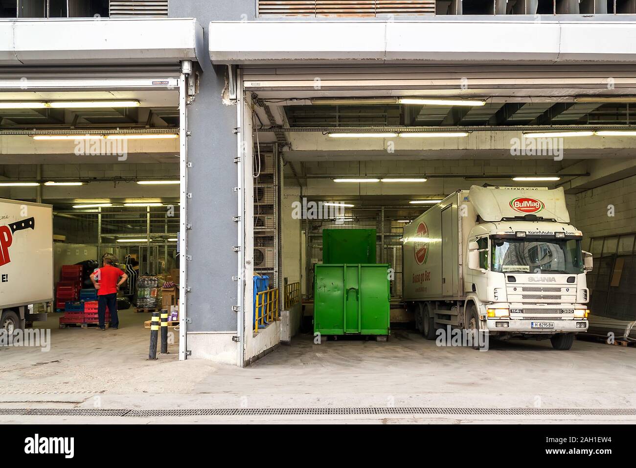 Varna, Bulgaria, December 20, 2019. Delivery area with opened rolling gates behind a supermarket and unloading goods from a white truck. Front view. Stock Photo