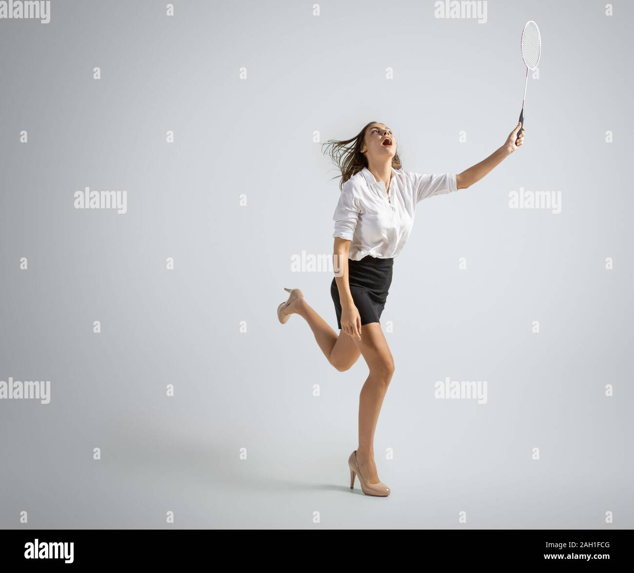 Time for fun and happiness. Woman in office clothes playing badminton on  grey studio background. Businesswoman training in motion, action. Unusual  look for sport, new activity. Sport, healthy lifestyle Stock Photo -