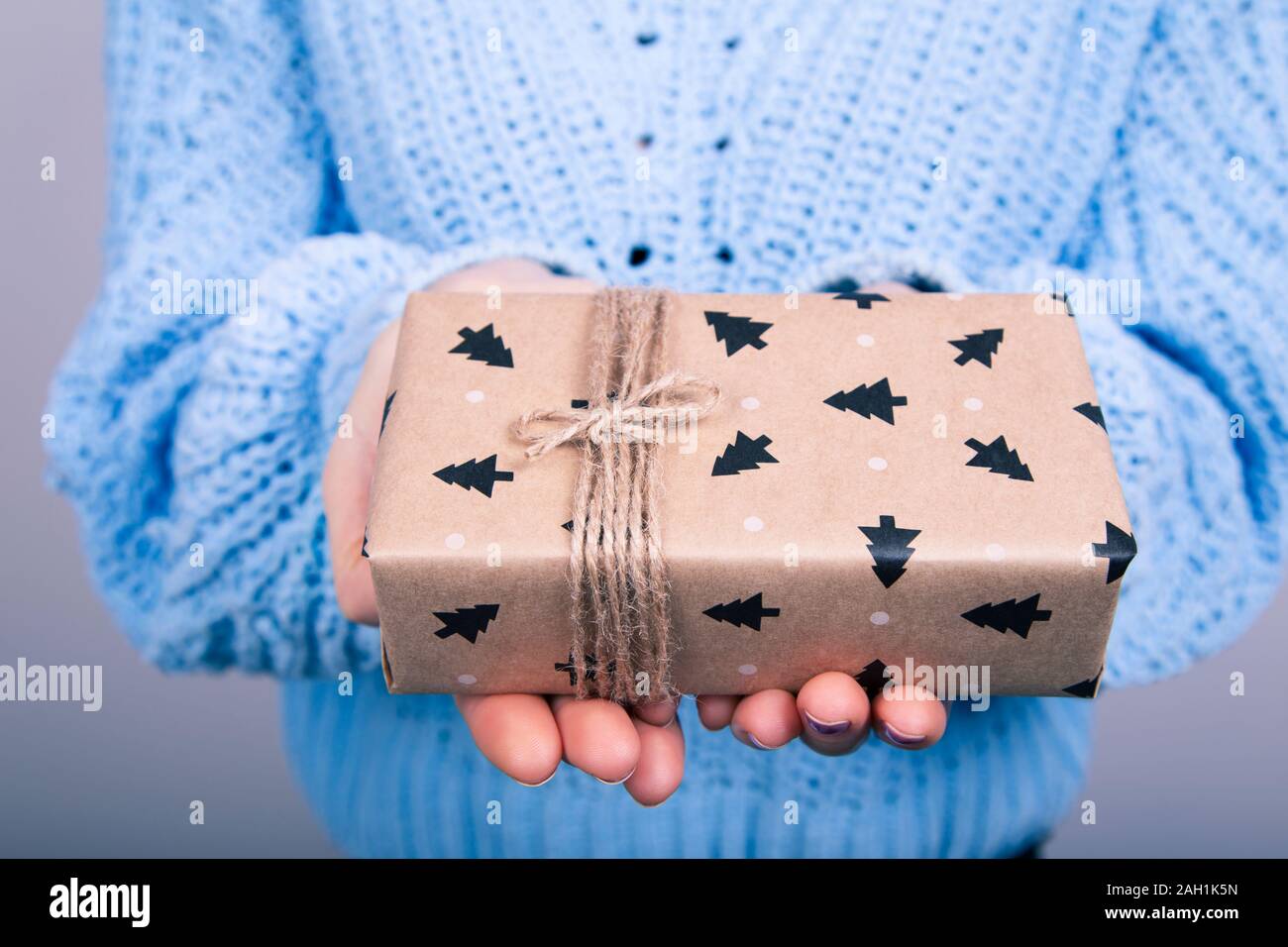Woman's hands in blue jumper holding craft paper gift box with a present for Christmas, new year, valentine day or anniversary on black background, to Stock Photo