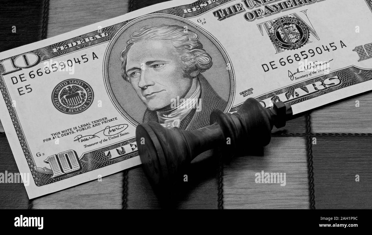 Business Concept: Defeated King Chess Piece Lying On A 10 Dollars Banknote On A Wooden Chess Board, Black And White Stock Photo