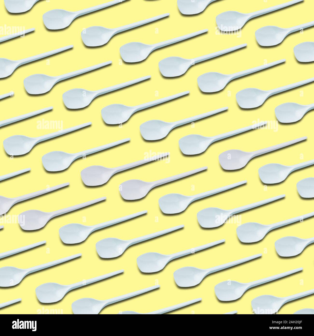 white plastic tea spoons pattern on yellow background Stock Photo