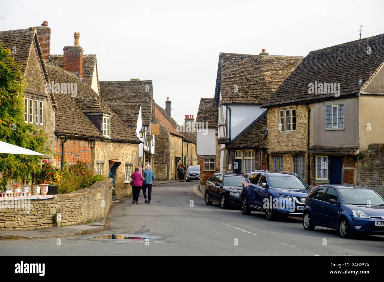 A senior couple walks arm in arm through the streets of Lacock, a small village with traditional houses. This location often serves as a movie set. Stock Photo