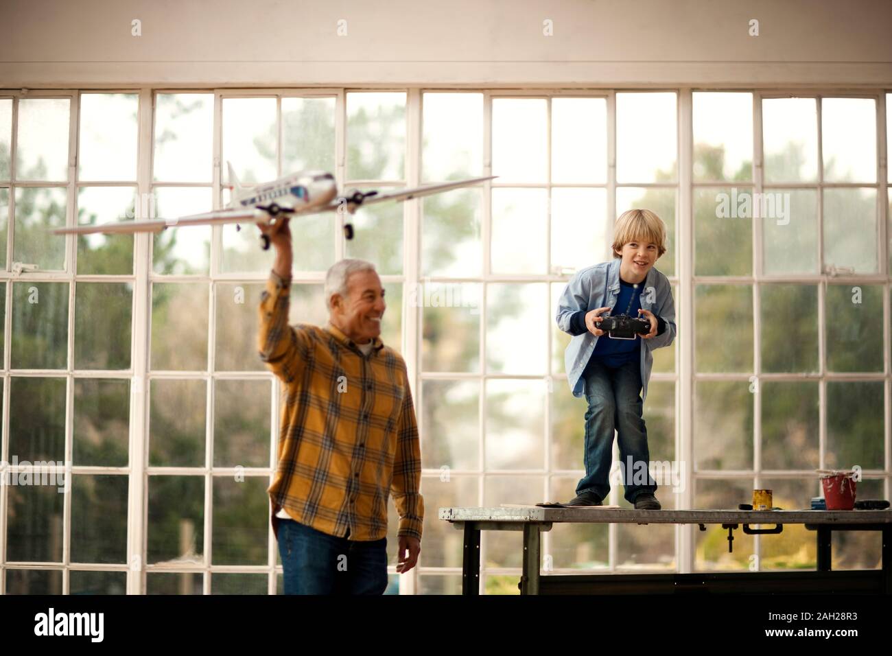 Smiling senior man and his grandson playing with a toy airplane together inside a garage. Stock Photo