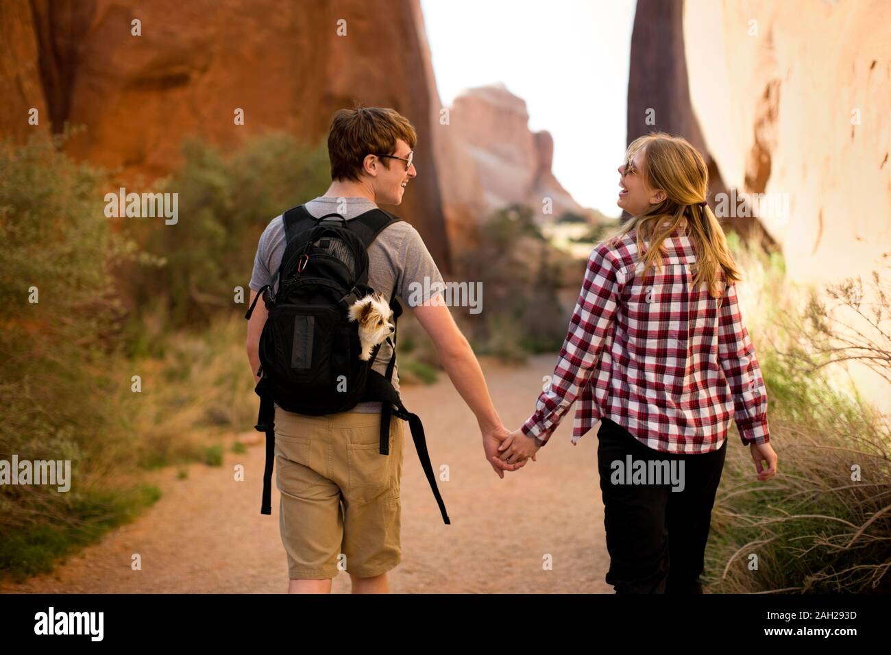 Happy young couple and their dog walking on a trail through rock ...