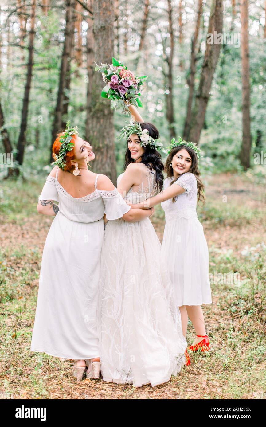 Bride and bridesmaids in white dresses posing on the forest background  outdoors. Bride holding her wedding bouquet. Rustic wedding in the forest  Stock Photo