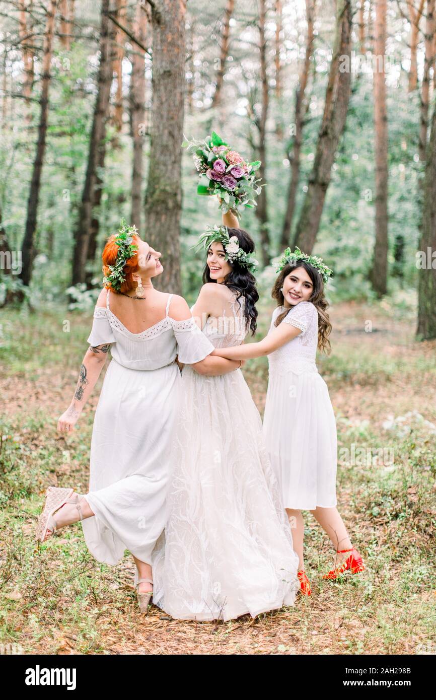 Two pretty bridesmaids surround bride with backs turned, full length  portrait on forest background. Women in white dresses and with floral  wreaths on Stock Photo - Alamy