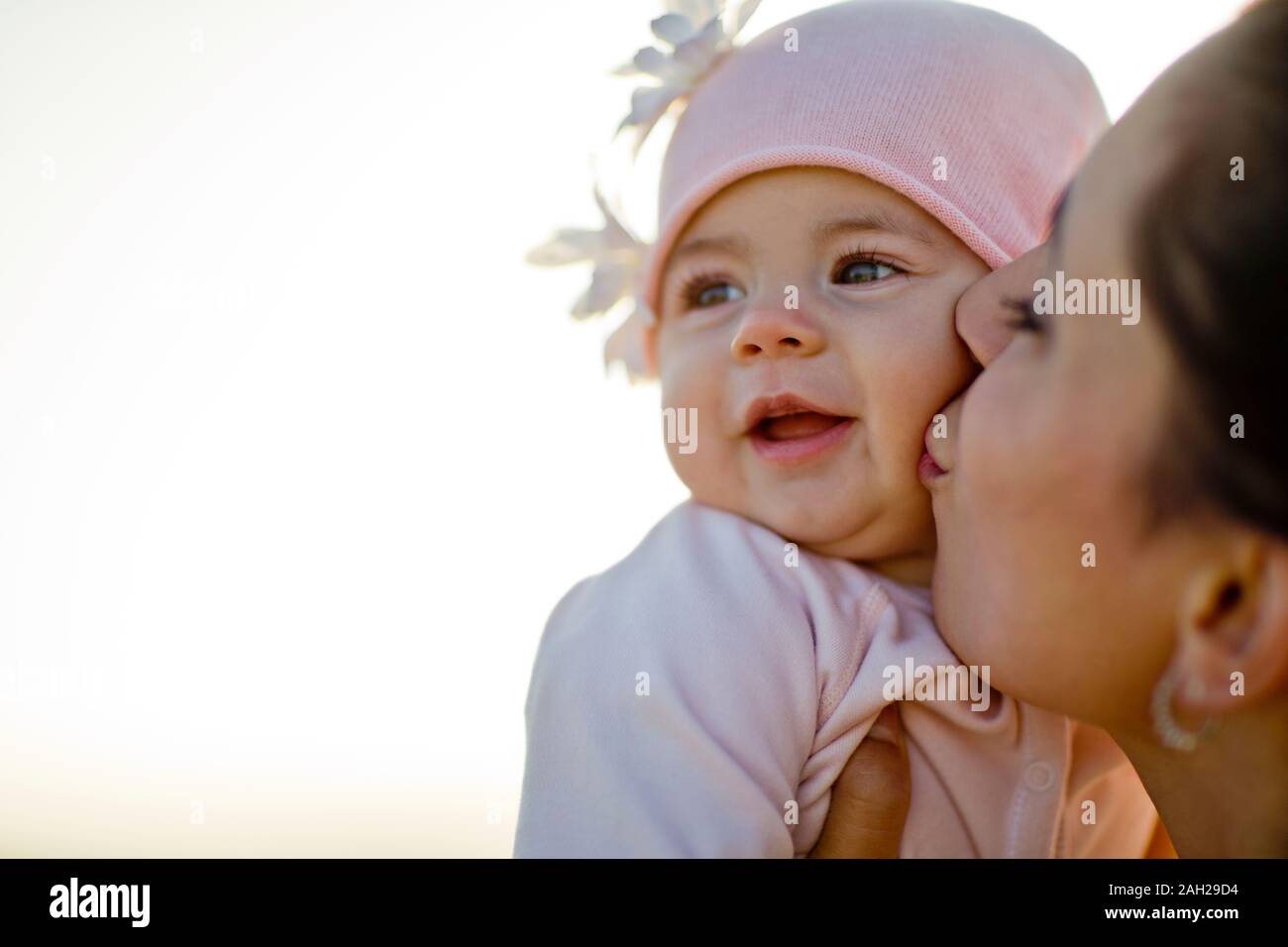 Mother kissing her smiling baby daughter on the cheek Stock Photo