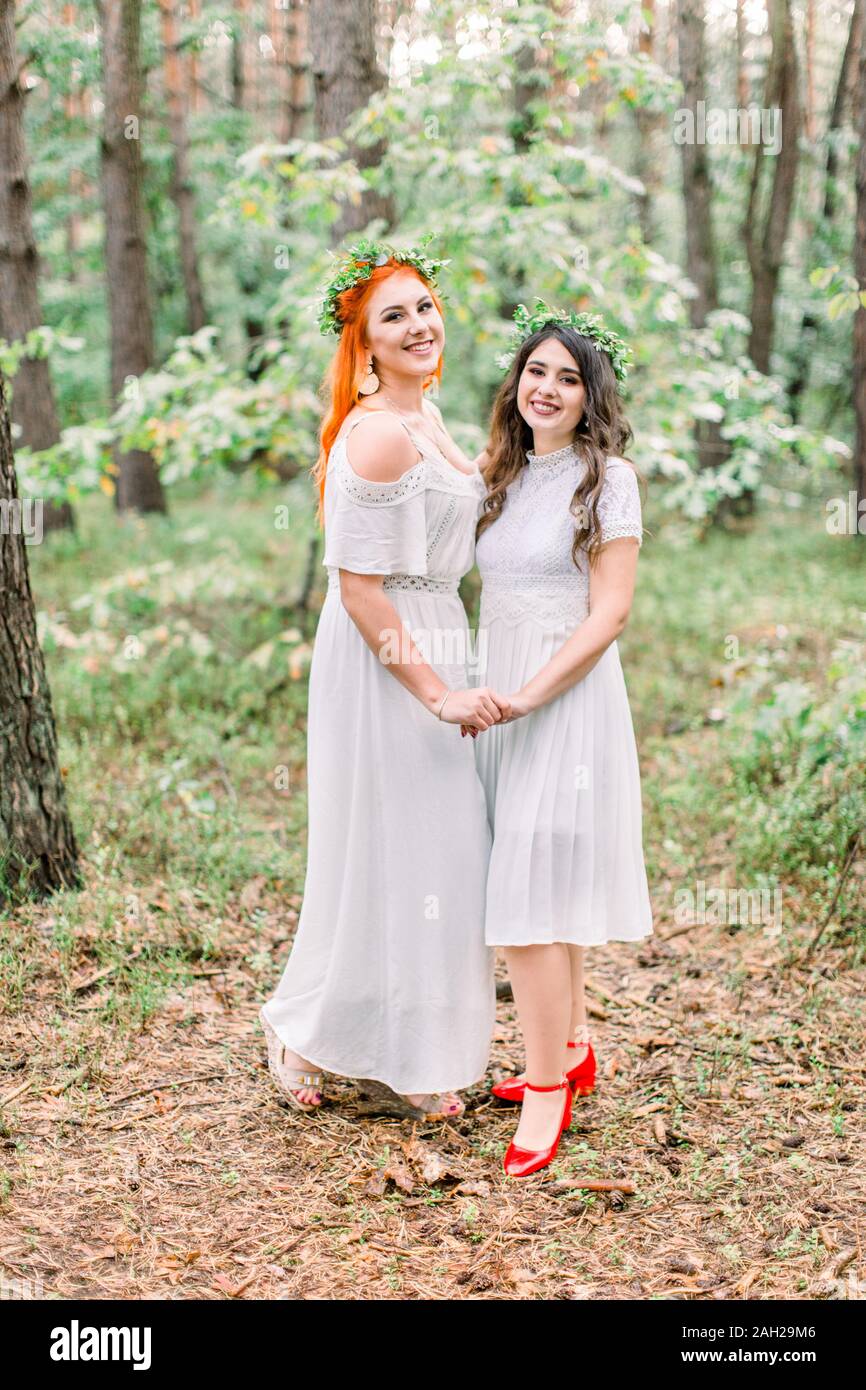 Two beautiful stylish happy bridesmaids in white dresses and wreaths on ...