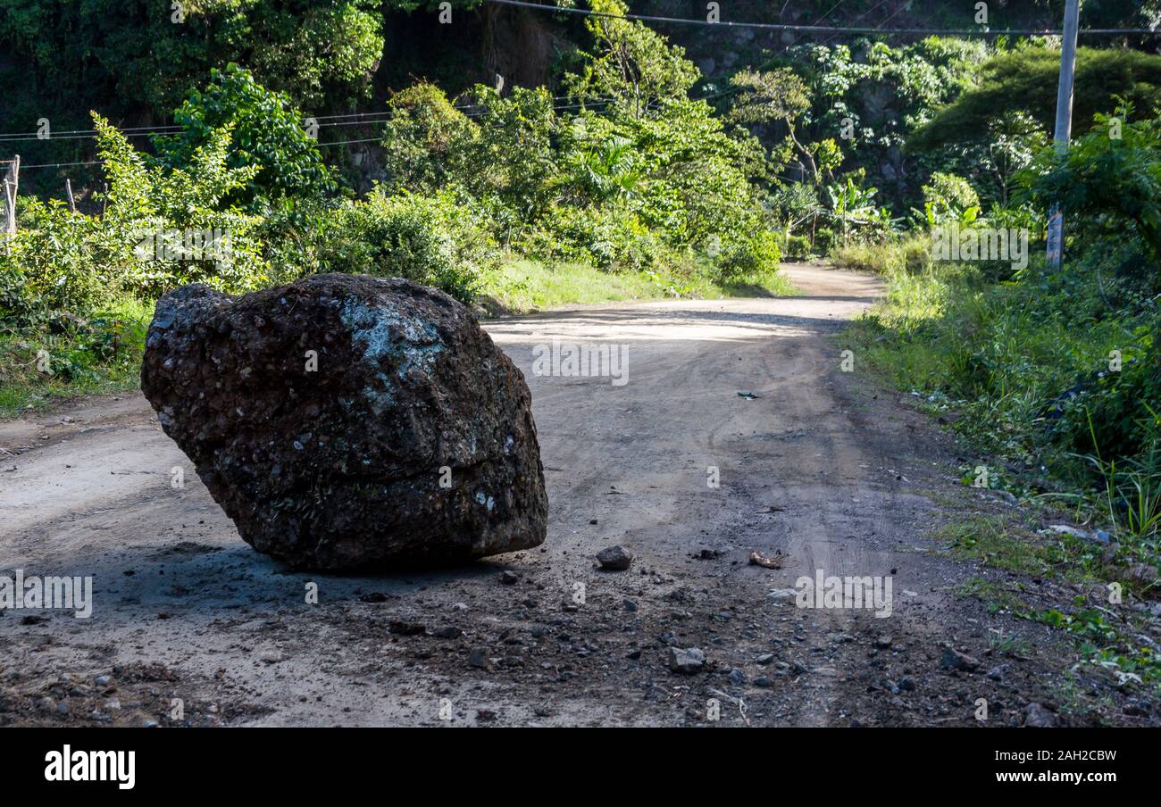 dramatic image of a fallen large rock in the middle of a dirt road in the caribbean mountains of the dominican republic. Stock Photo