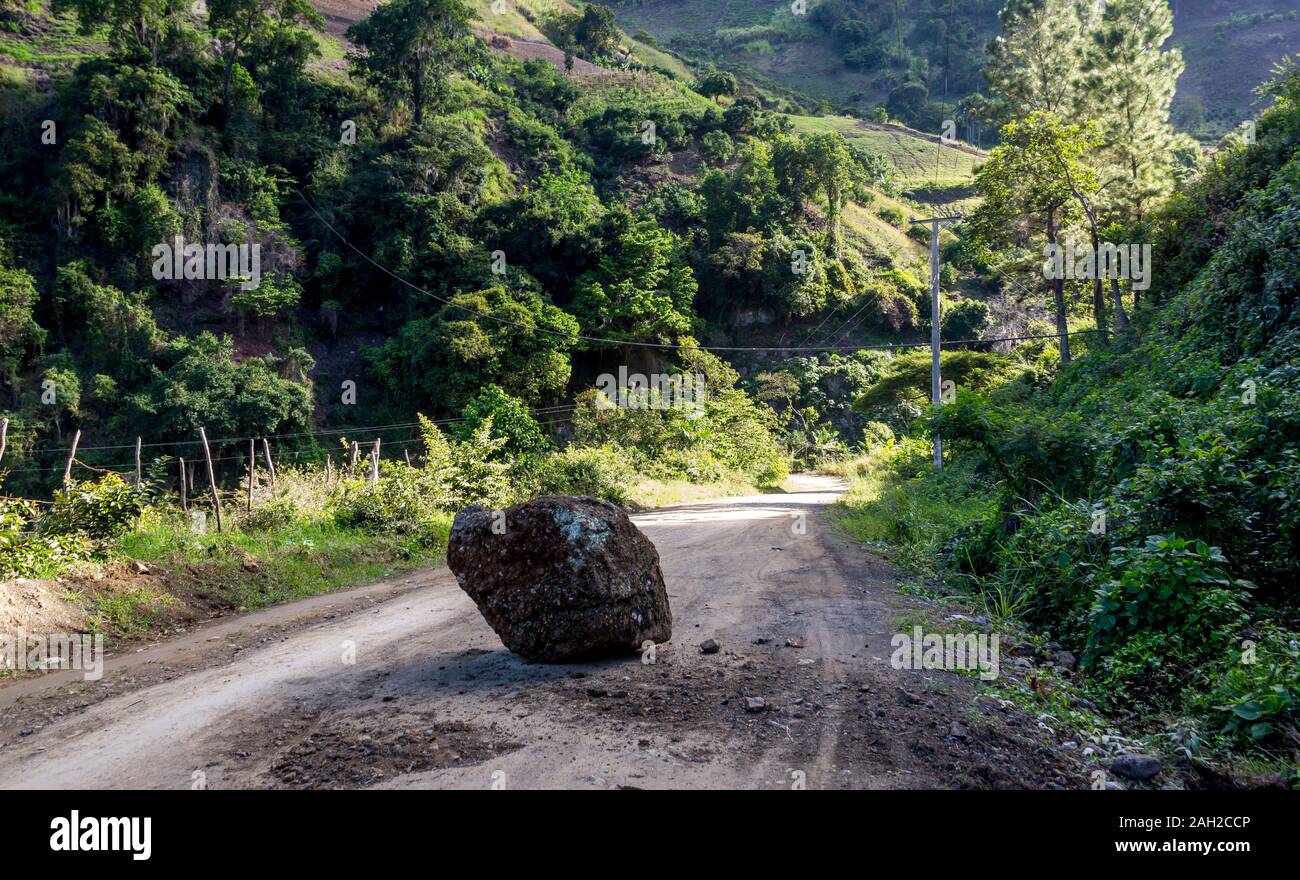 dramatic image of a fallen large rock in the middle of a dirt road in the caribbean mountains of the dominican republic. Stock Photo