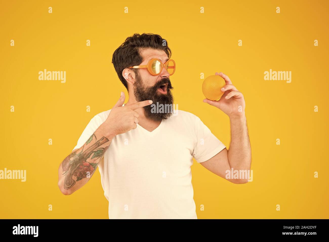 A citrus food. Hipster pointing finger at vitamin food on yellow background. Bearded man with healthy organic food. Vegan food and diet. Stock Photo