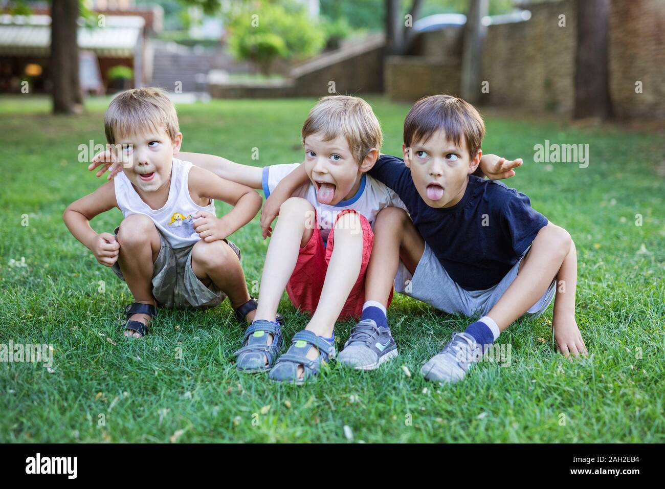 Three young boys making weird grimace faces in summer park. Friends or siblings having fun outdoors. Stock Photo
