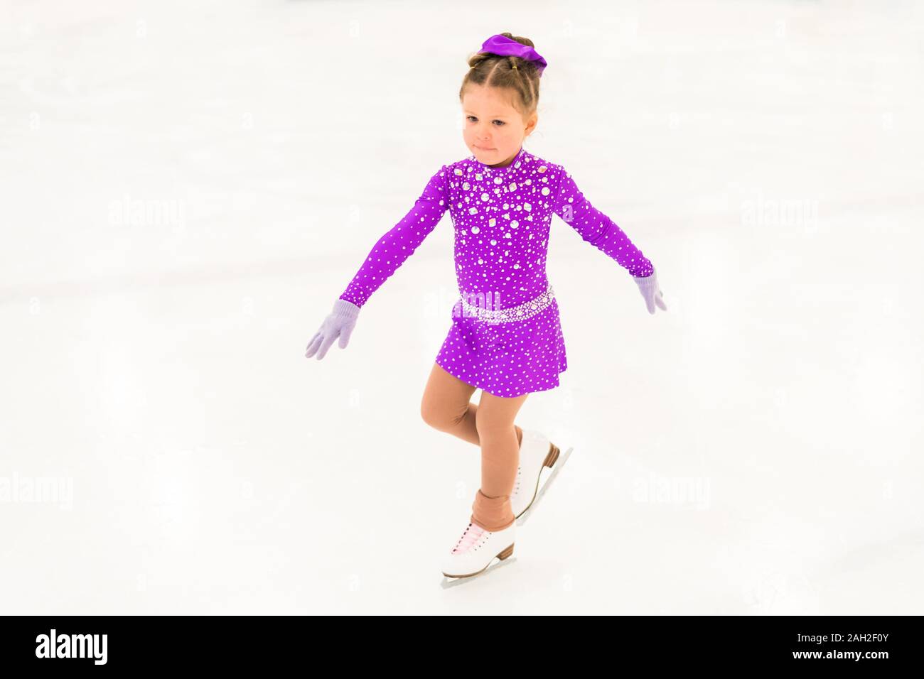 Little girl practicing figure skating in a purple dress with crystals