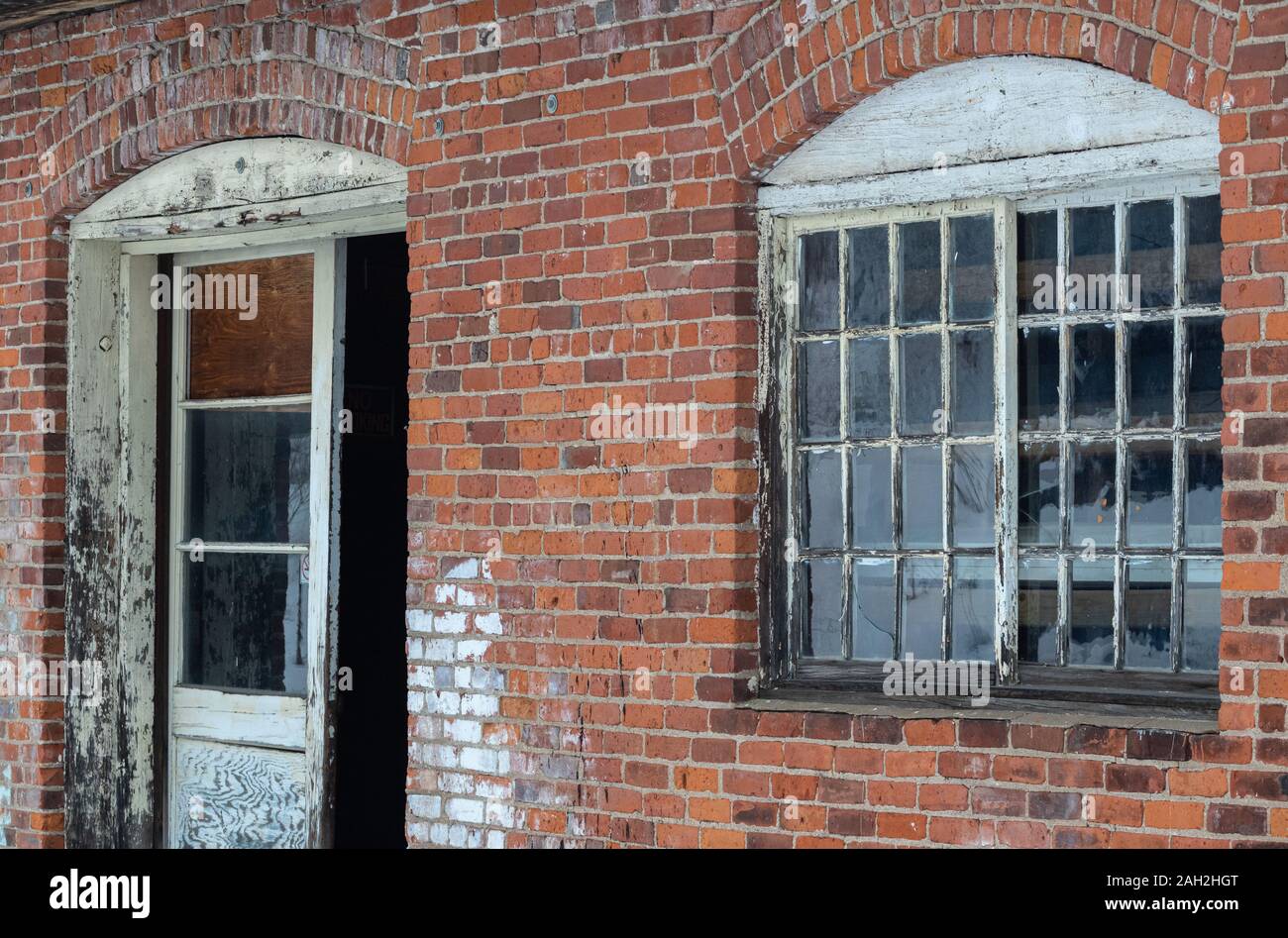 Textures and features of an old exterior brick wall with windows and wooden door. Stock Photo