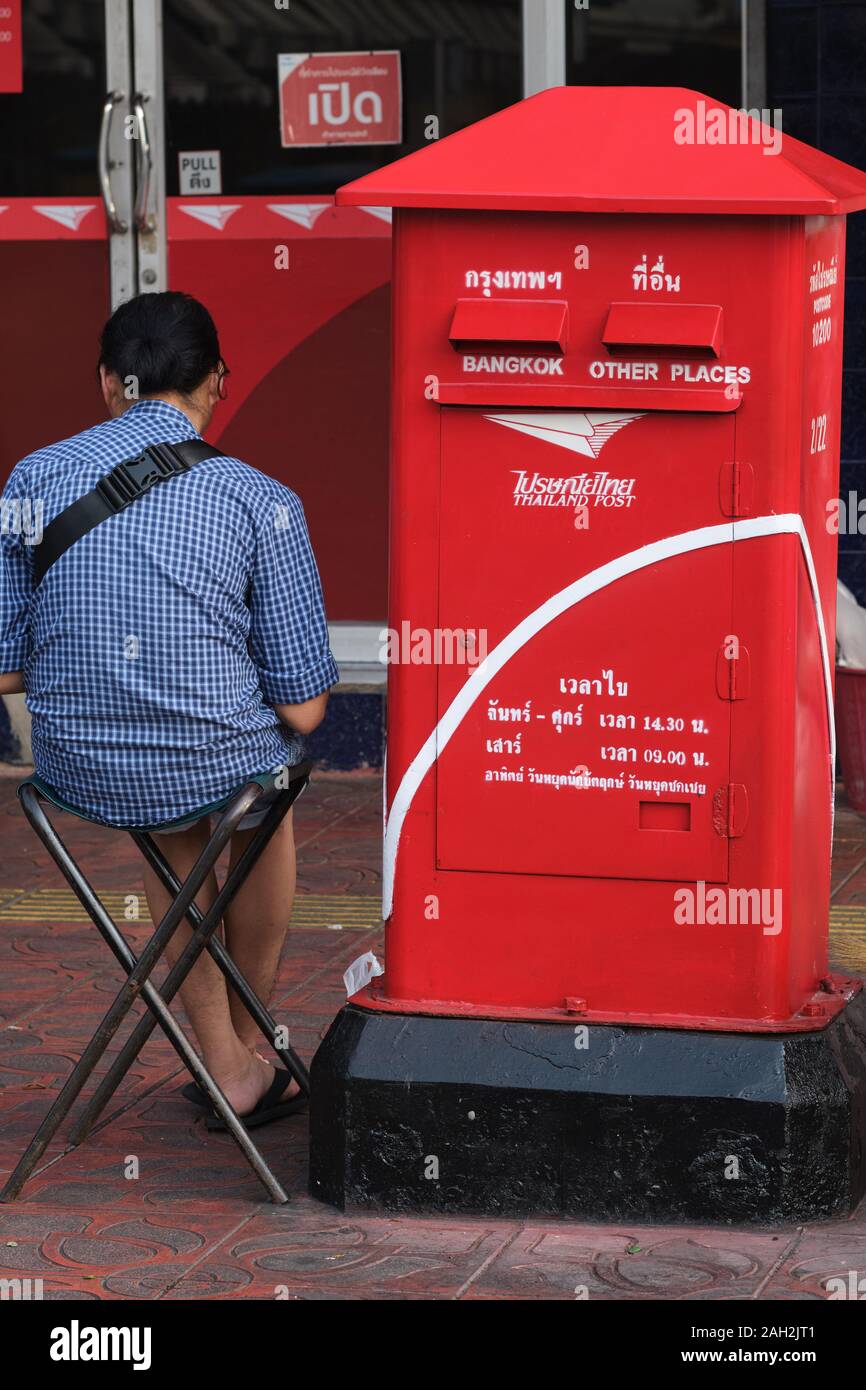 A lottery vendor sitting in front of a post office next to a red letter-box in Bangkok, Thailand Stock Photo