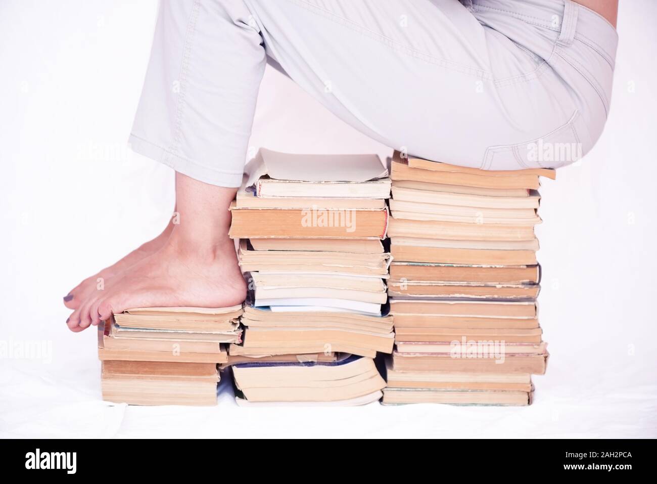 Young girl sitting on a stack of old books Stock Photo - Alamy
