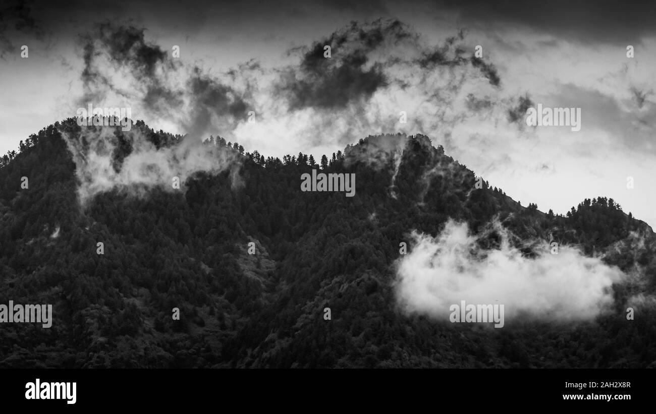 Panoramic view of low hanging white clouds in front of a mountain with dark moody sky Stock Photo