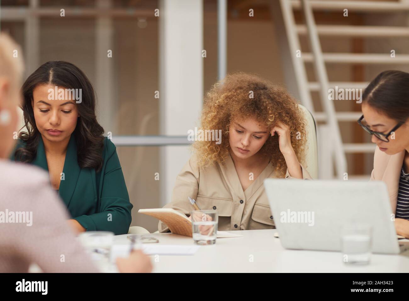 Horizontal eye level shot of pensive young businesswomen doing their job together sitting at office table Stock Photo