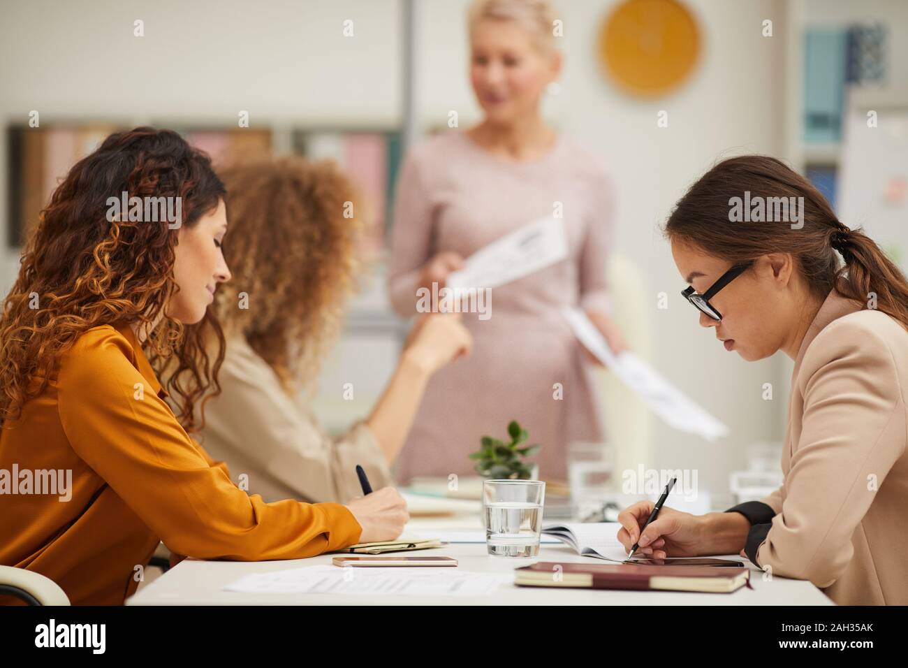 Businesswomen making notes while their middle-aged colleague demonstration her presentation, horizontal eye level shot Stock Photo