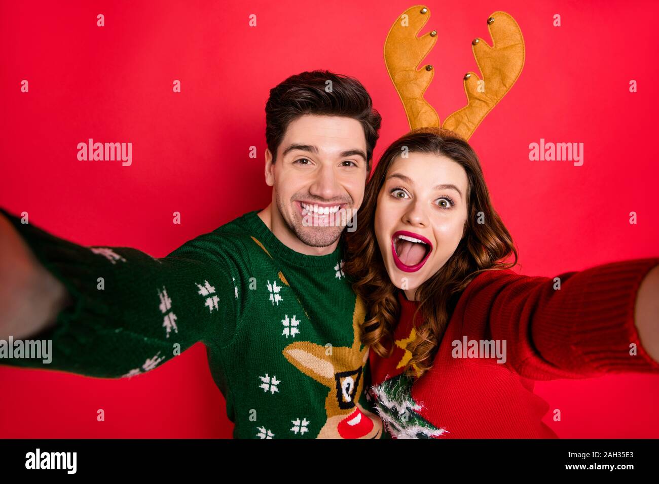 Photo of crazy lady and guy at x-mas costume party making selfies wear knitted jumpers with ornament isolated red color background Stock Photo