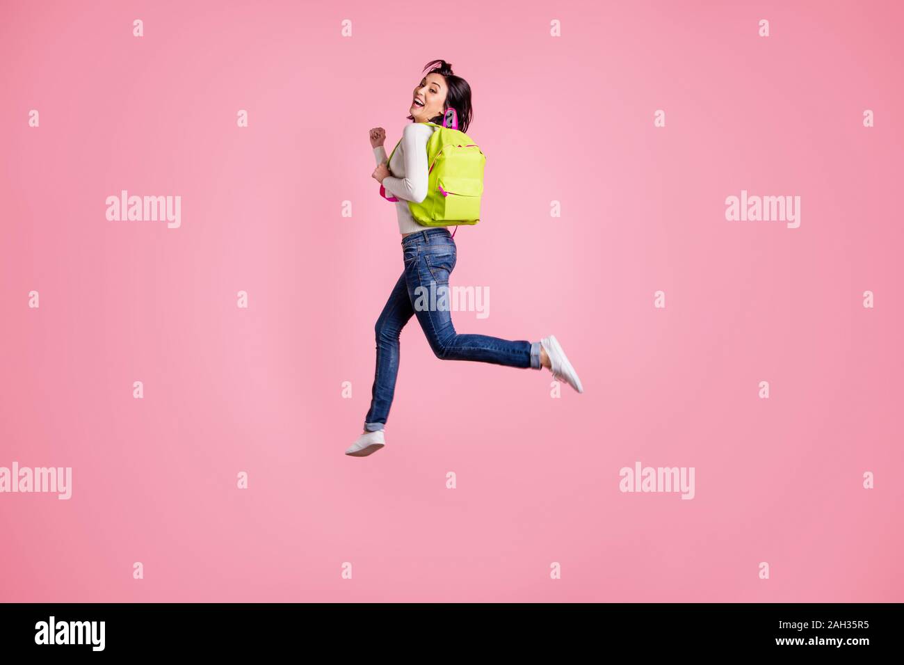 Full body photo of crazy lady jumping high holding green rucksack running autumn sale shopping wear pullover and jeans isolated pink color background Stock Photo