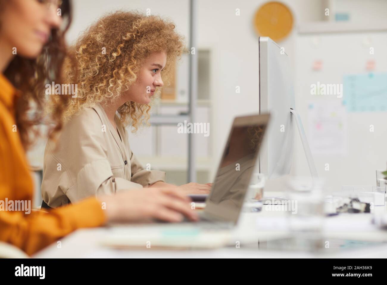 Two young women with curly hair working on modern computers in office side view shot Stock Photo