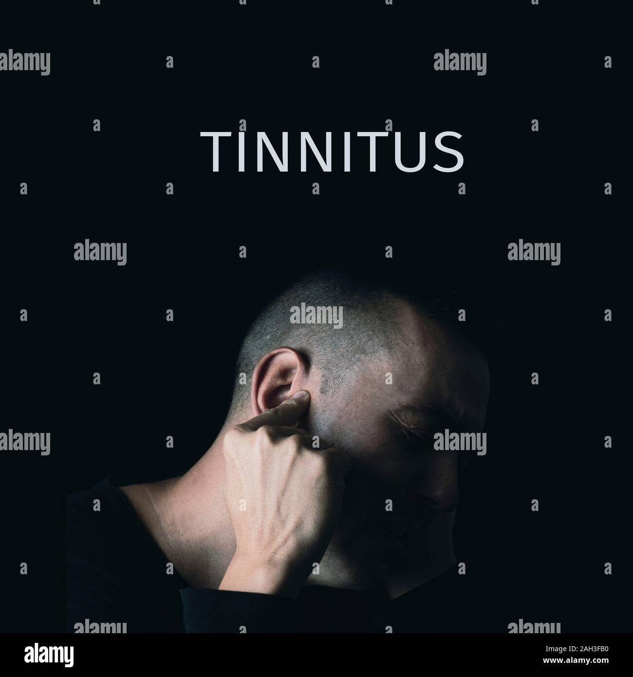 closeup of a suffering caucasian man pressing his ear with his forefinger, and the text tinnitus on a black background Stock Photo