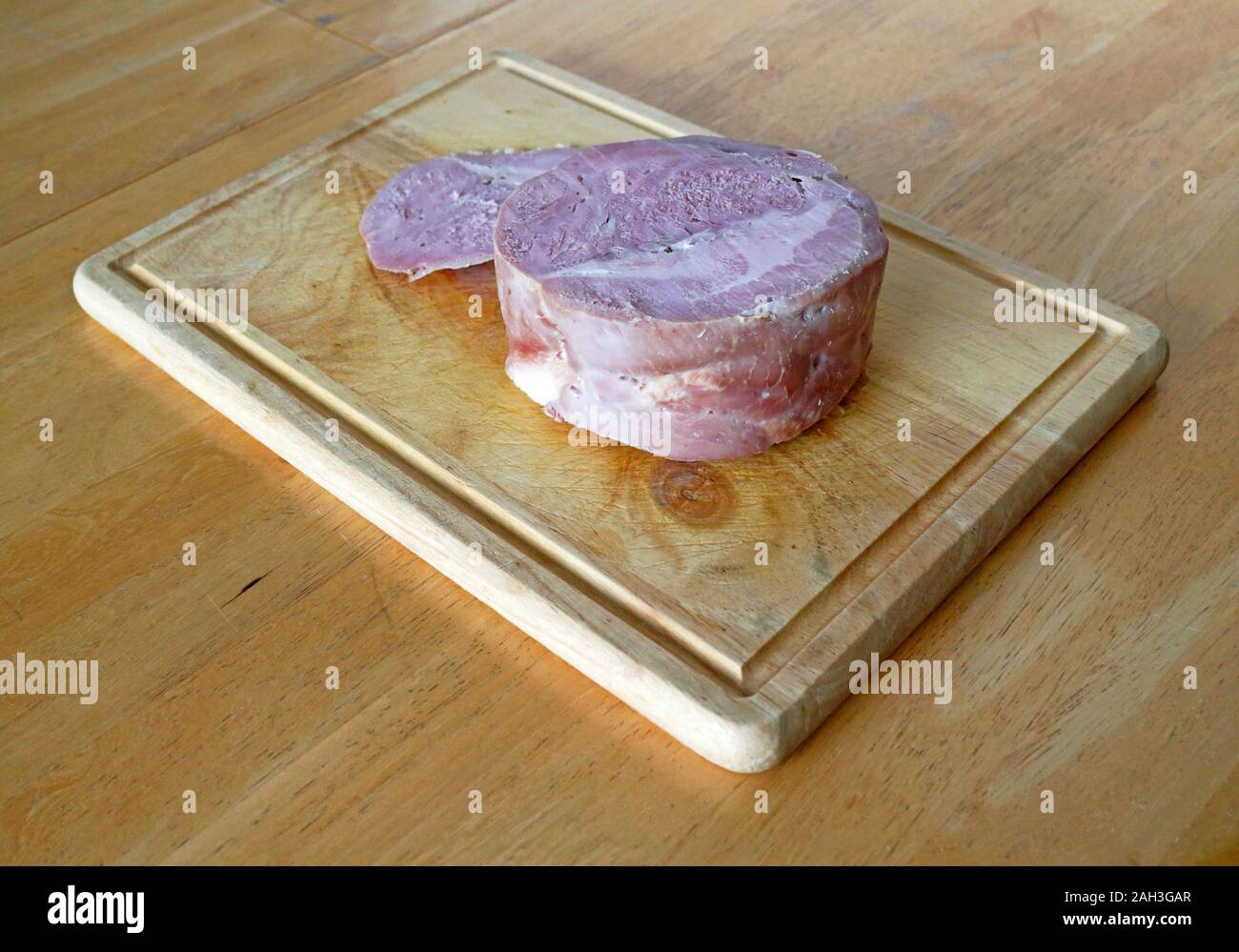 A freshly home cooked smoked gammon joint with one slice by the side on a wooden chopping board. Stock Photo