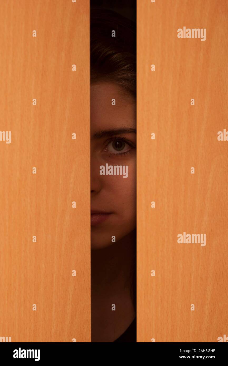 young woman or girl peeking from behind a door partially opened Stock Photo