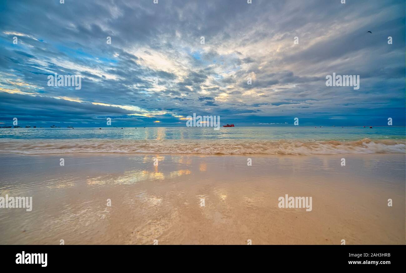 On a beach of the Caribbean Sea. The first rays of the sun illuminate the fishing boats. The partly cloudy sky and the transparent and calm sea. Stock Photo