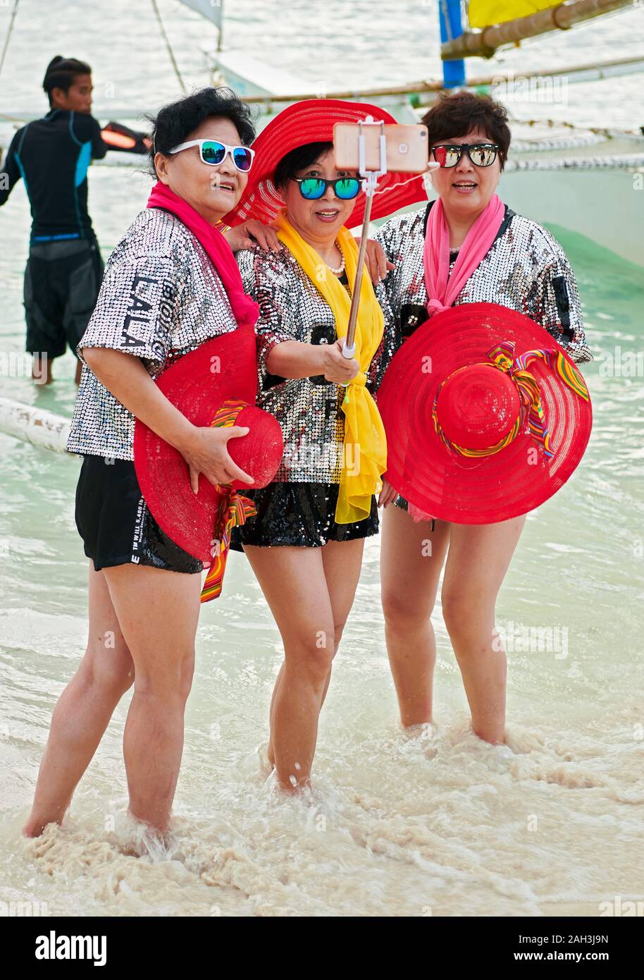 Boracay, Aklan Province, Philippines - January 6 2018: Three Chinese women tourists in colorful attire posing for a group picture with their mobile ph Stock Photo