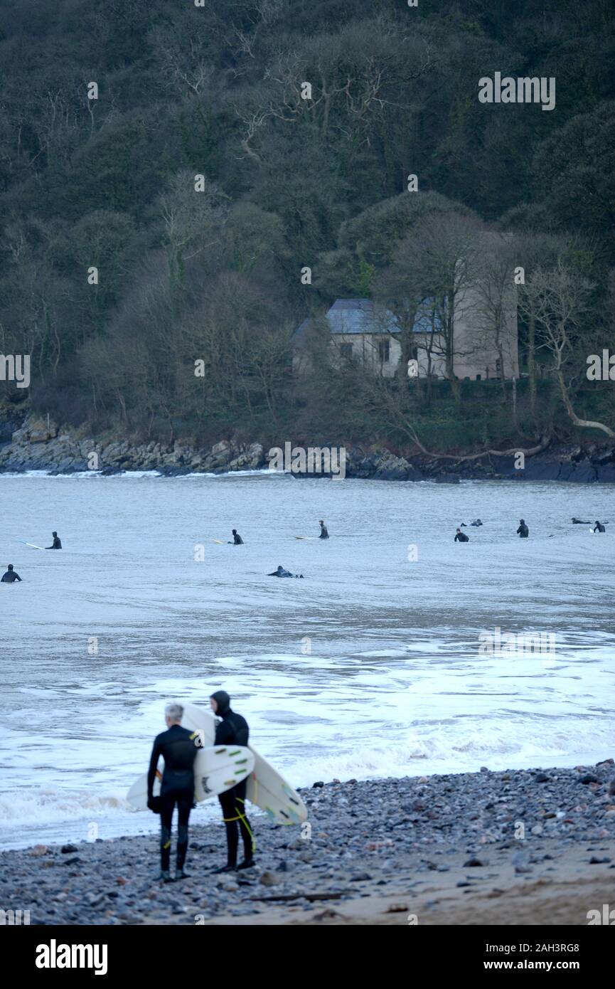 Surfers at Oxwich Bay with St Illtyds church in woodland background