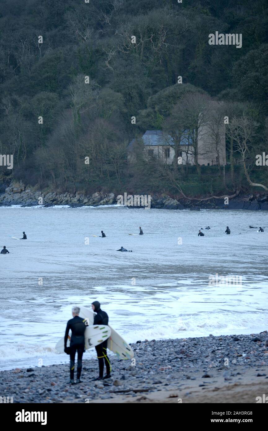 Surfers at Oxwich Bay with St Illtyds church in woodland background, Gower Stock Photo