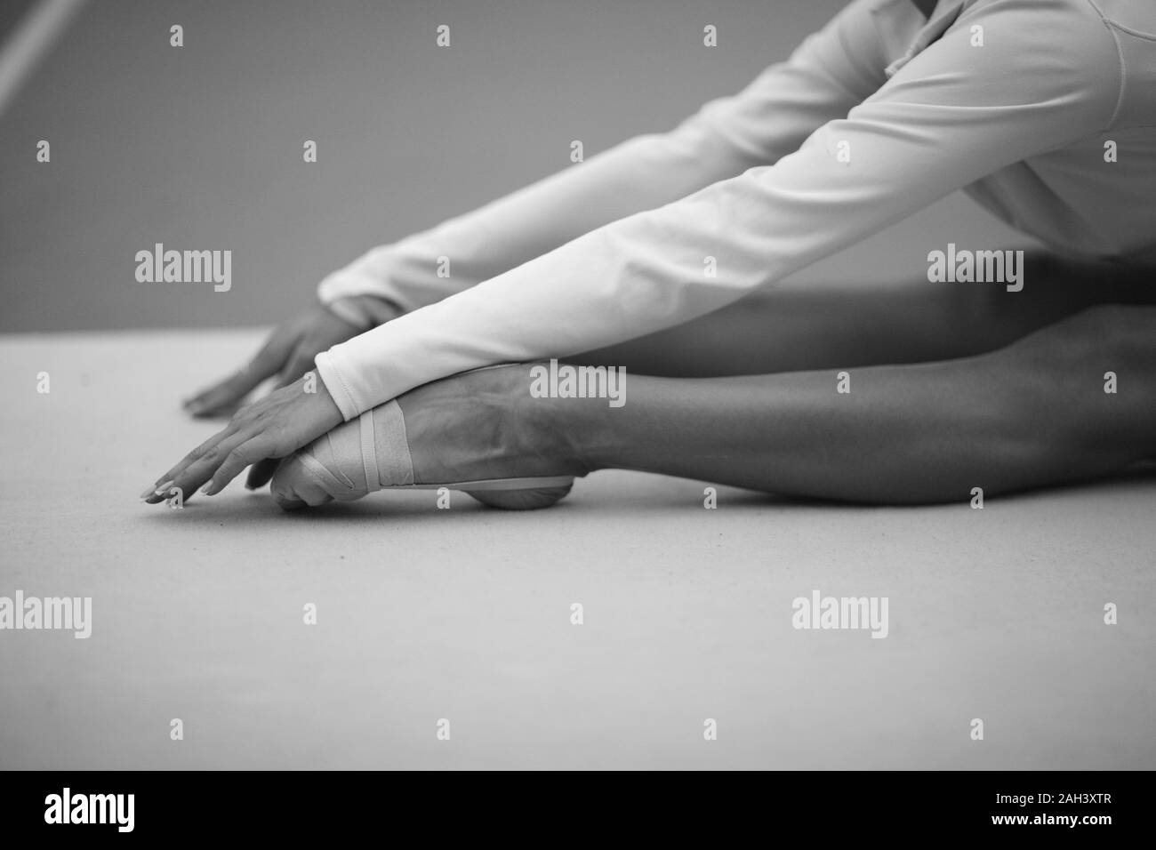 The stretched arms and legs of a gymnast sitting on the floor in a