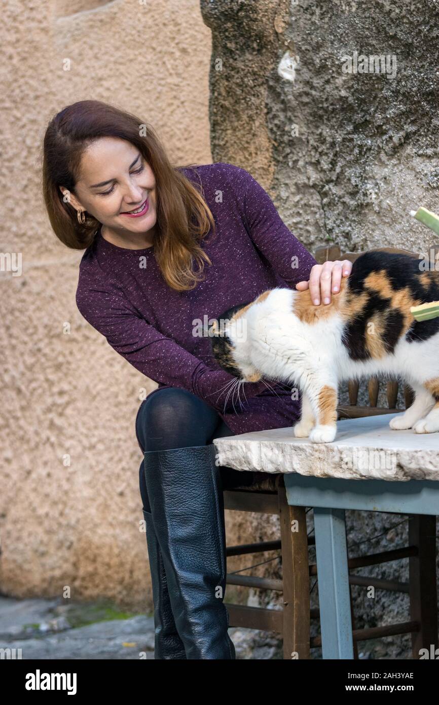 Portrait of a mature woman wearing high knee black boots and a purple dress, caressing a cat. Stock Photo