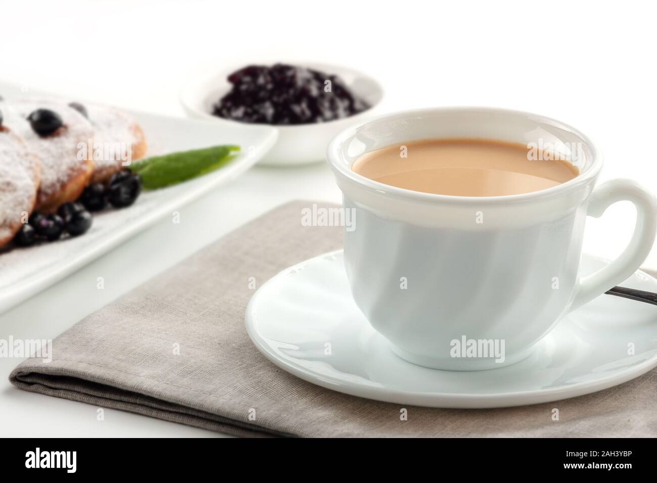 Cup of coffee with milk and a plate with pancakes on a white table. Stock Photo