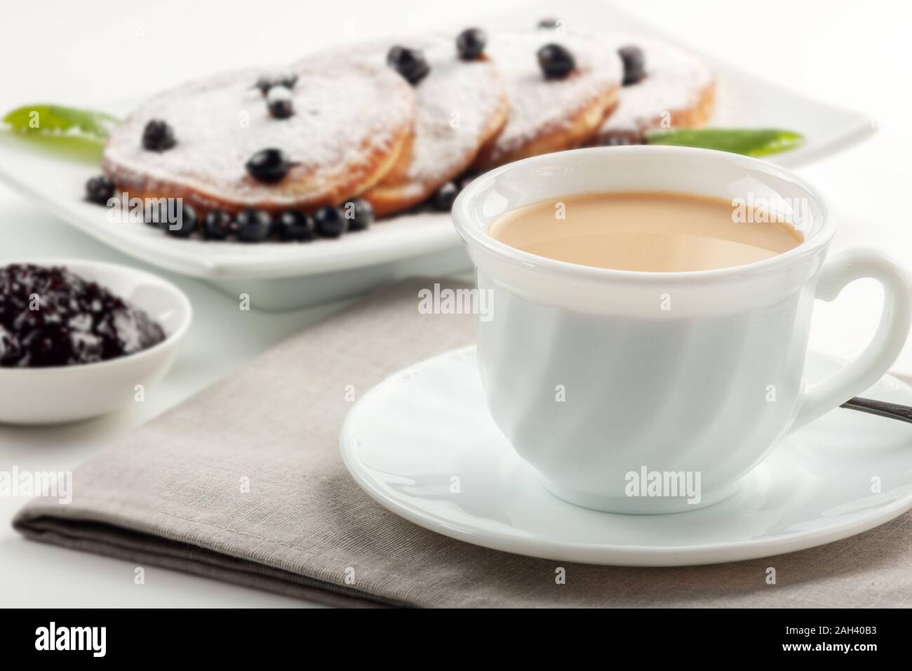 Cup of coffee with milk and a plate with pancakes on a white table. Stock Photo