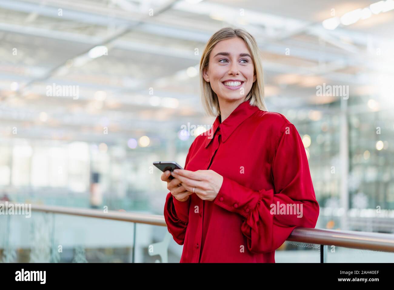 Smiling young businesswoman standing at a railing with cell phone Stock Photo