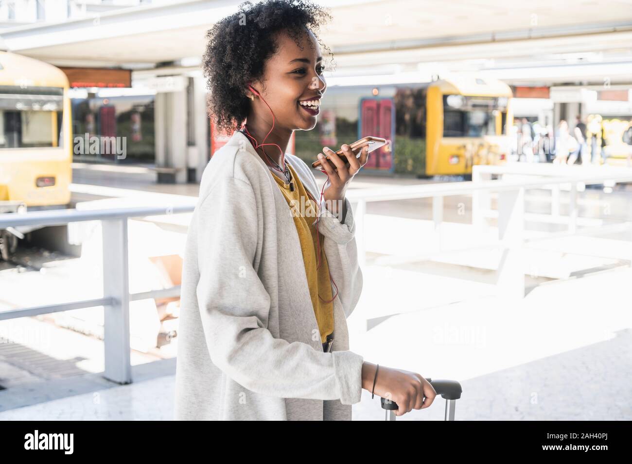 Happy young woman with earphones using smartphone at station platform Stock Photo