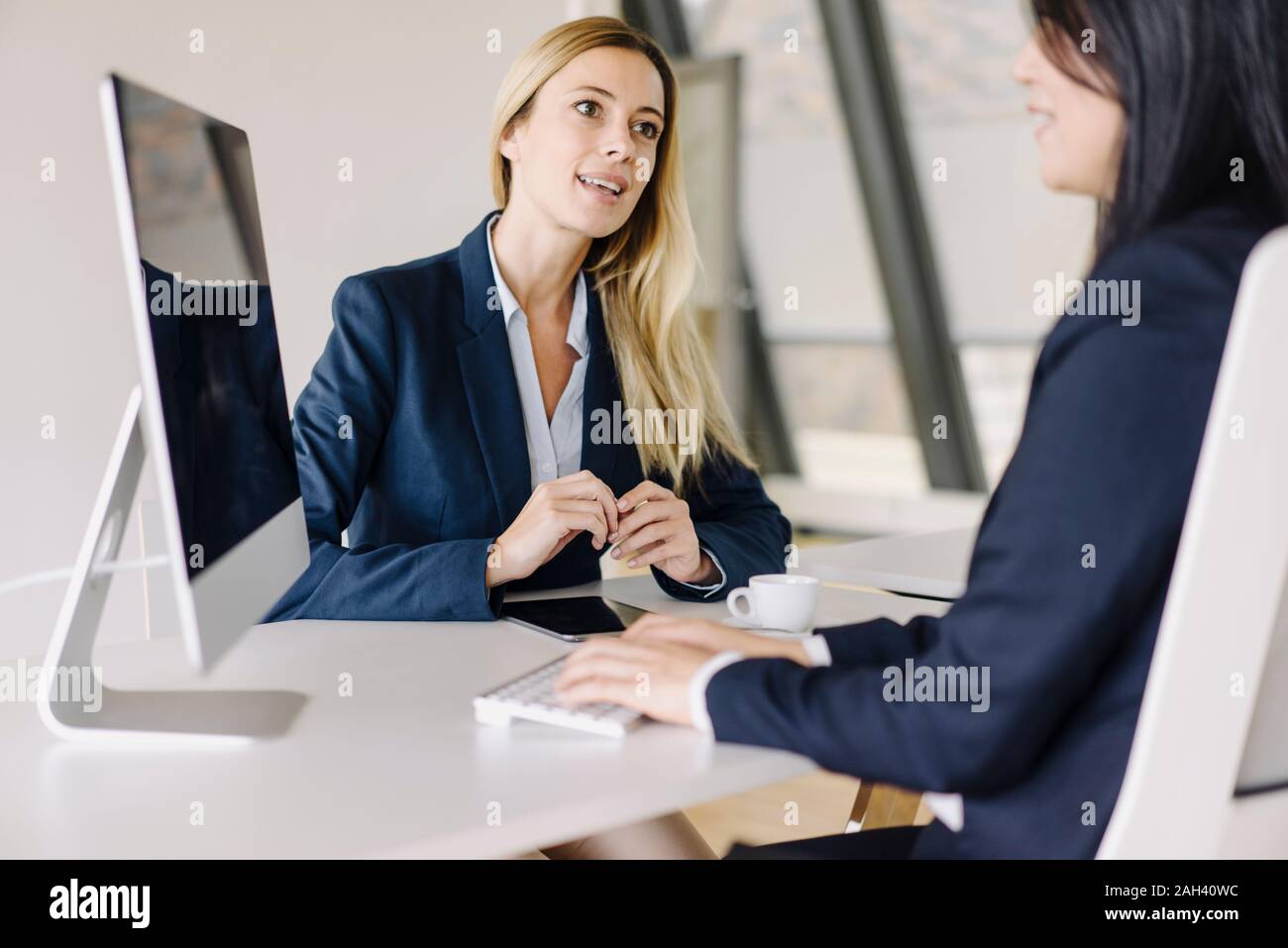 Two businesswomen sitting at desk in office talking Stock Photo