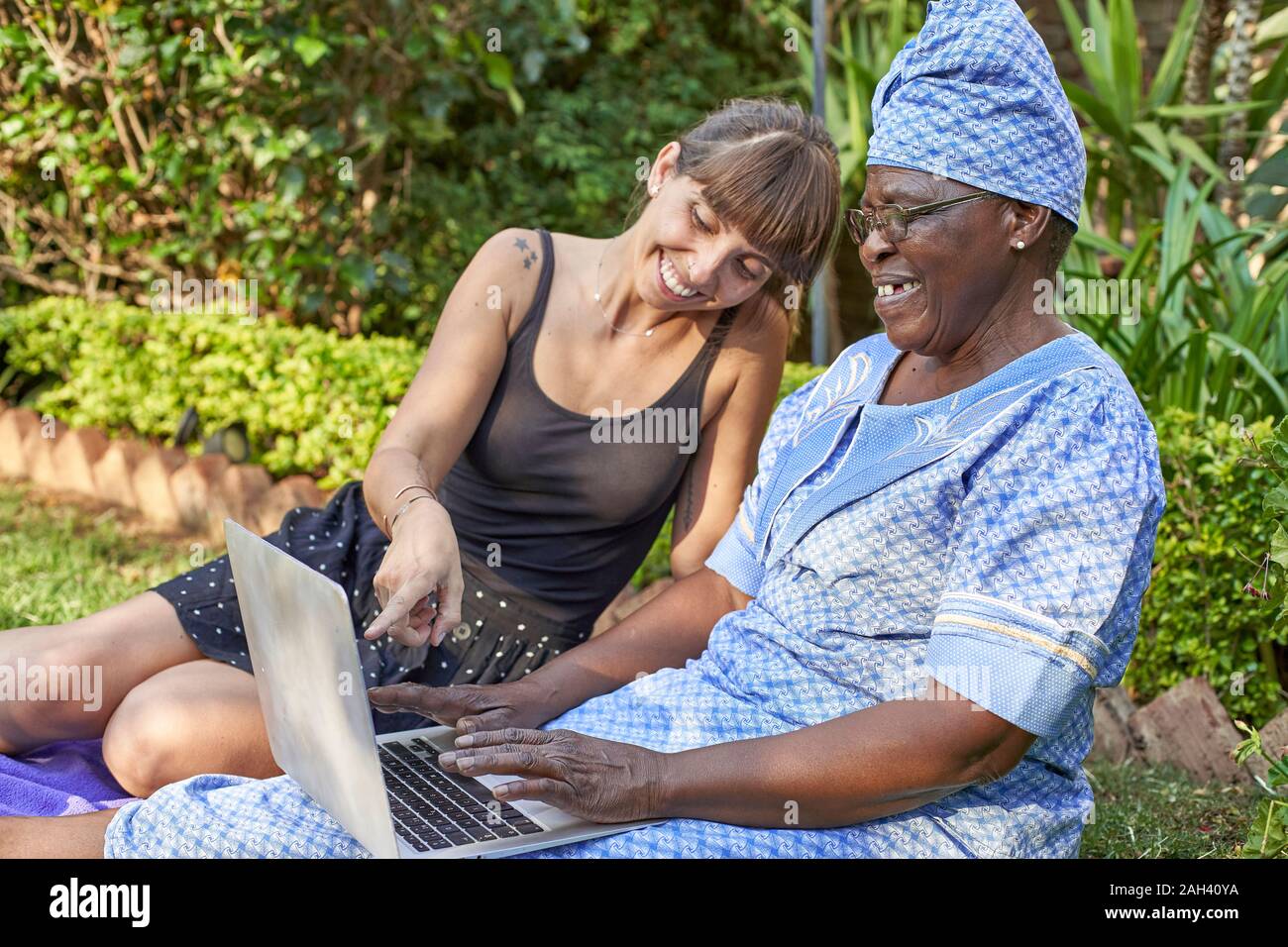 Happy senior woman sitting on lawn sharing laptop with a woman Stock Photo