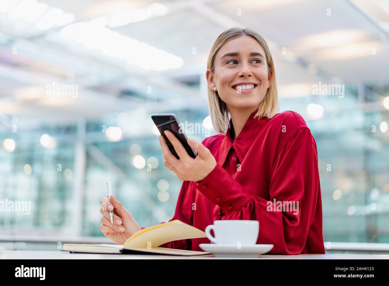 Young businesswoman with cell phone taking notes in a cafe Stock Photo