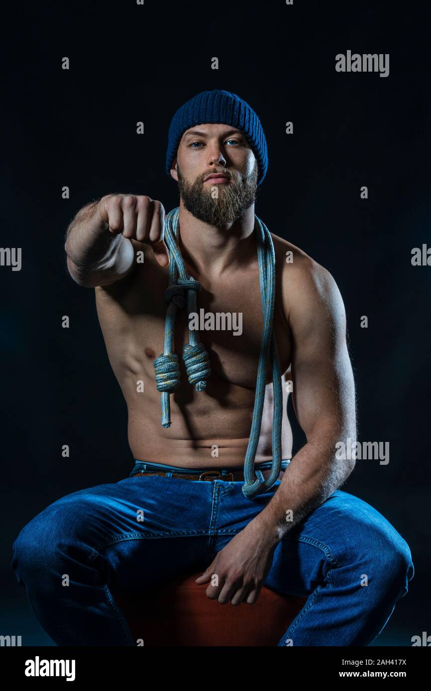 Portrait of a barechested athlete with skipping rope sitting clenching fist in studio Stock Photo