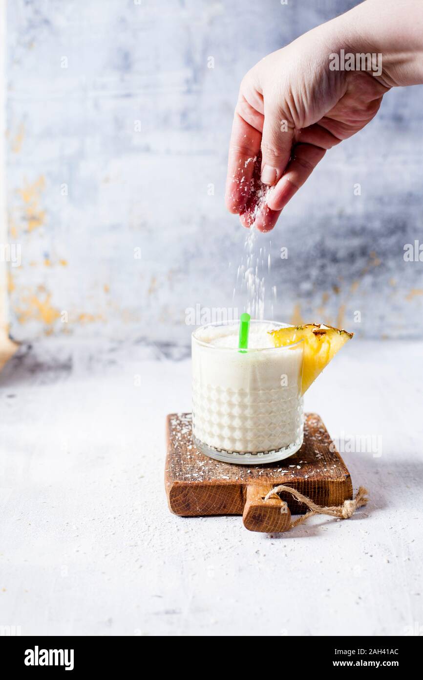 Woman scattering coconut flakes on a pineapple coconut smoothie Stock Photo