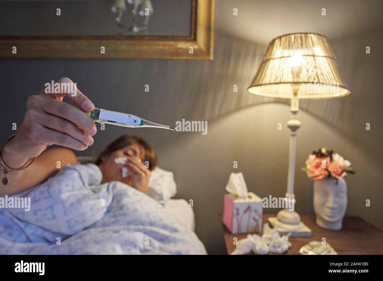 Sick woman laying in the bed and checking her temperature on the thermometer Stock Photo