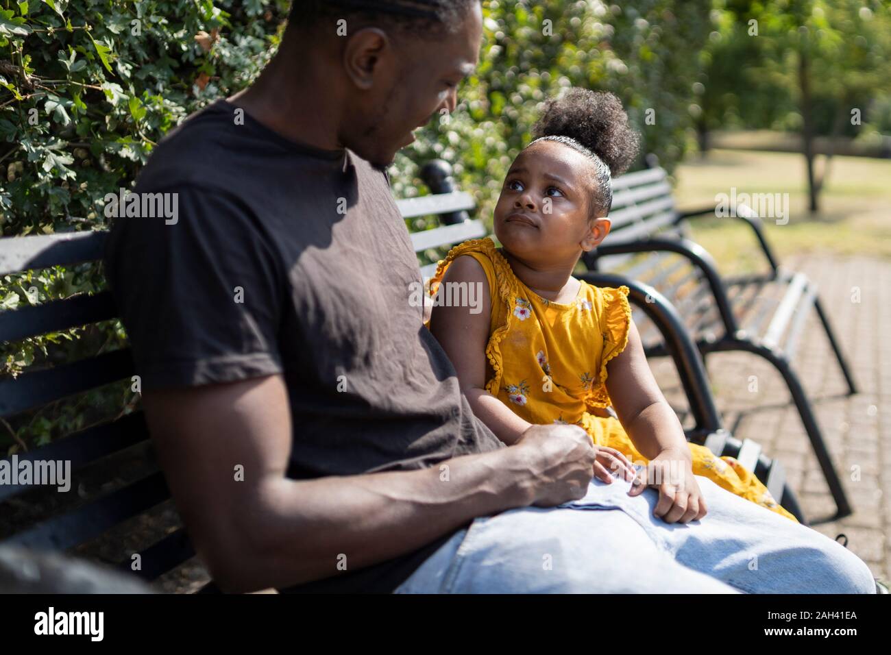 Father and daughter sitting on a bench in a park Stock Photo - Alamy